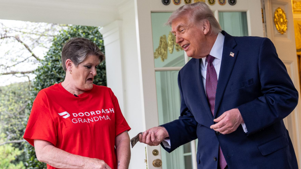 Donald Trump hands tip to a woman wearing a red shirt that says "DoorDash Grandma."