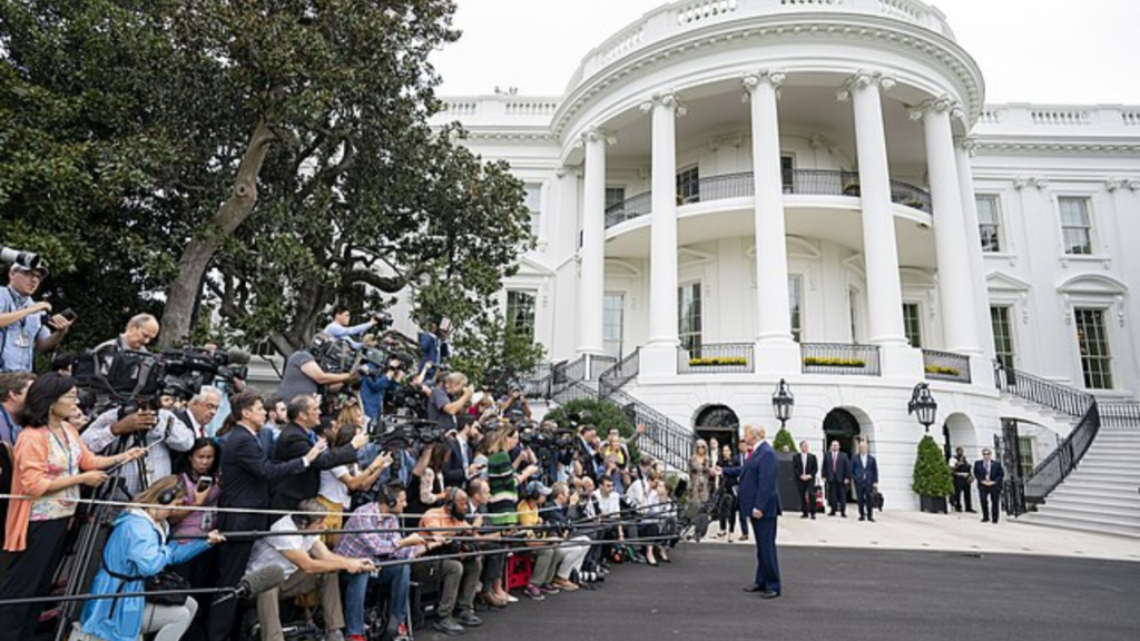A large group of reporters with cameras and microphones gathers around Donald Trump outside the White House.