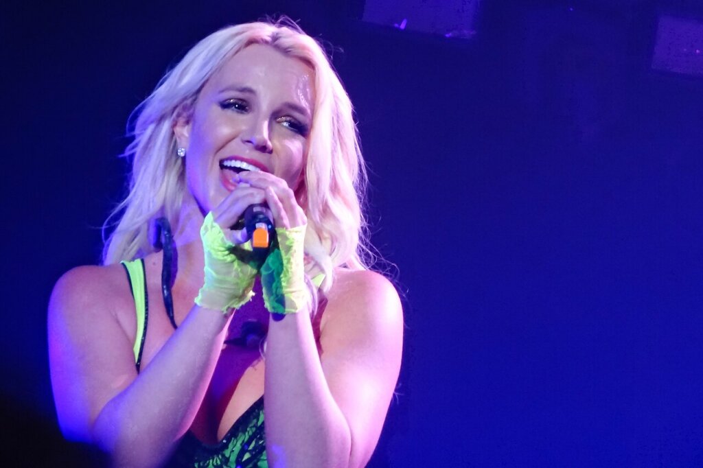 Britney singing into a handheld microphone under stage lights during a live performance.