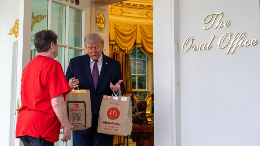 Donald Trump holds two McDonald's delivery bags while talking to a woman at the door of the Oval Office.
