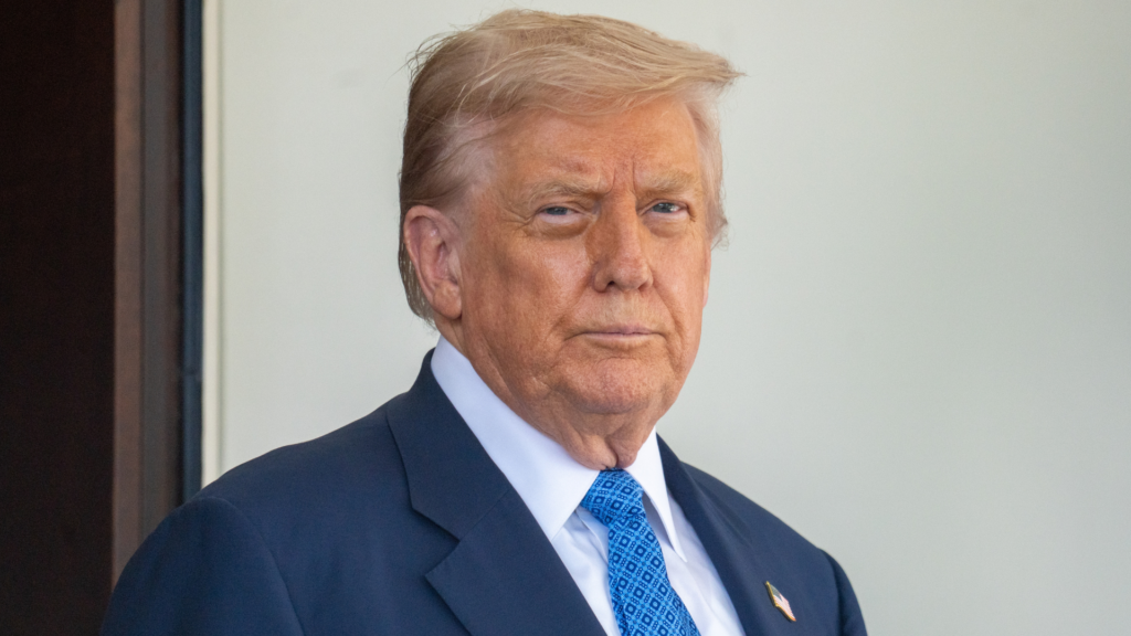 President Donald Trump standing outdoors in a navy suit and blue tie.