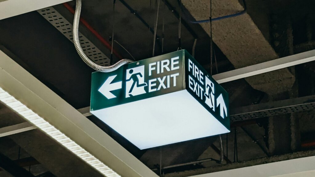 Ceiling-mounted fire exit sign with arrow inside a building.