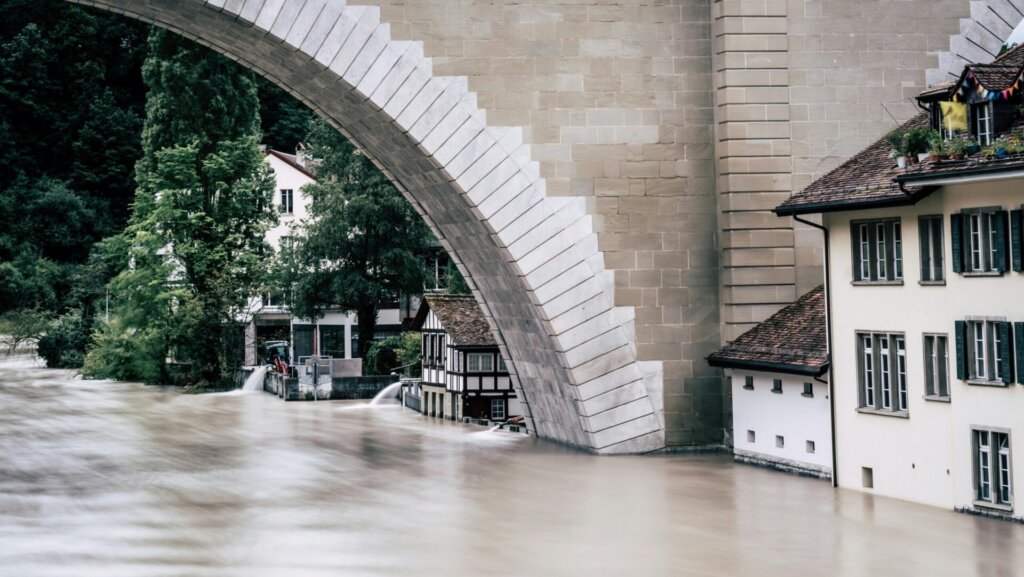Flooded river flowing under stone bridge with high water levels.