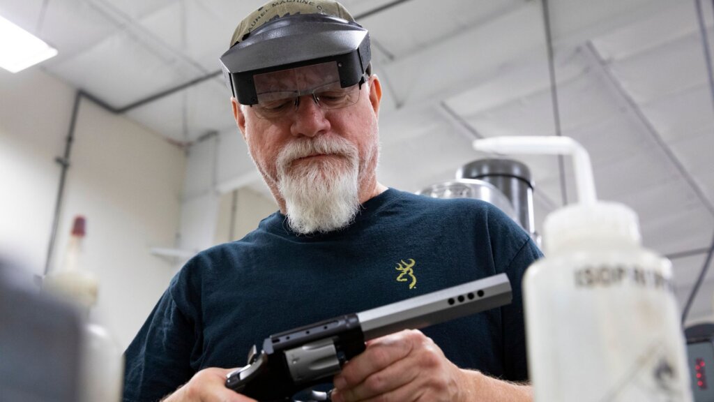 Factory worker inspecting a handgun component in a manufacturing facility.