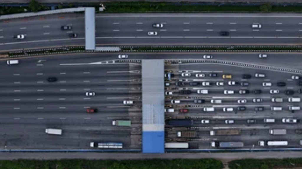 A top-down aerial view of a multi-lane highway leading into a large toll plaza or automated gantry.