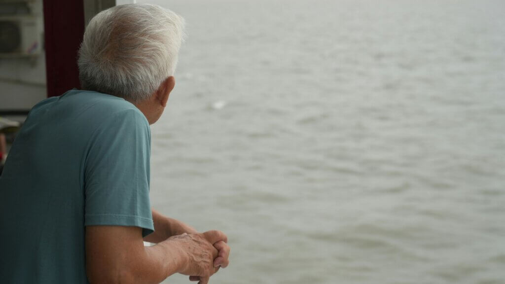 Older man leaning on a railing looking out over a body of water.