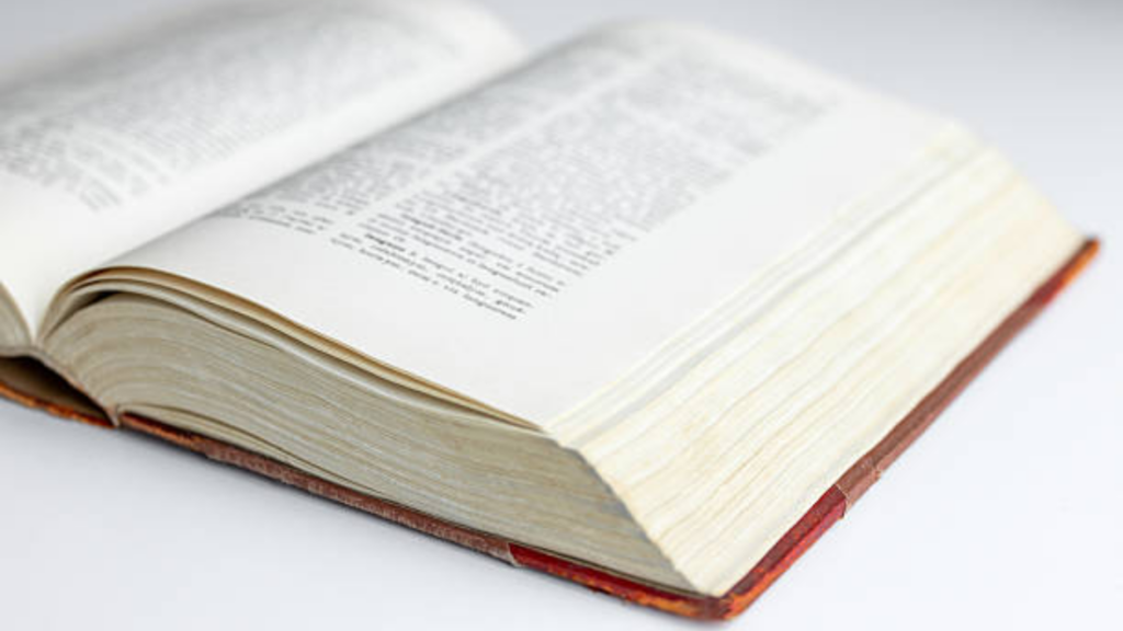 A close-up of an open, thick hardcover book with thin white pages and small black text, likely a Bible or legal tome, resting on a white surface with soft focus.