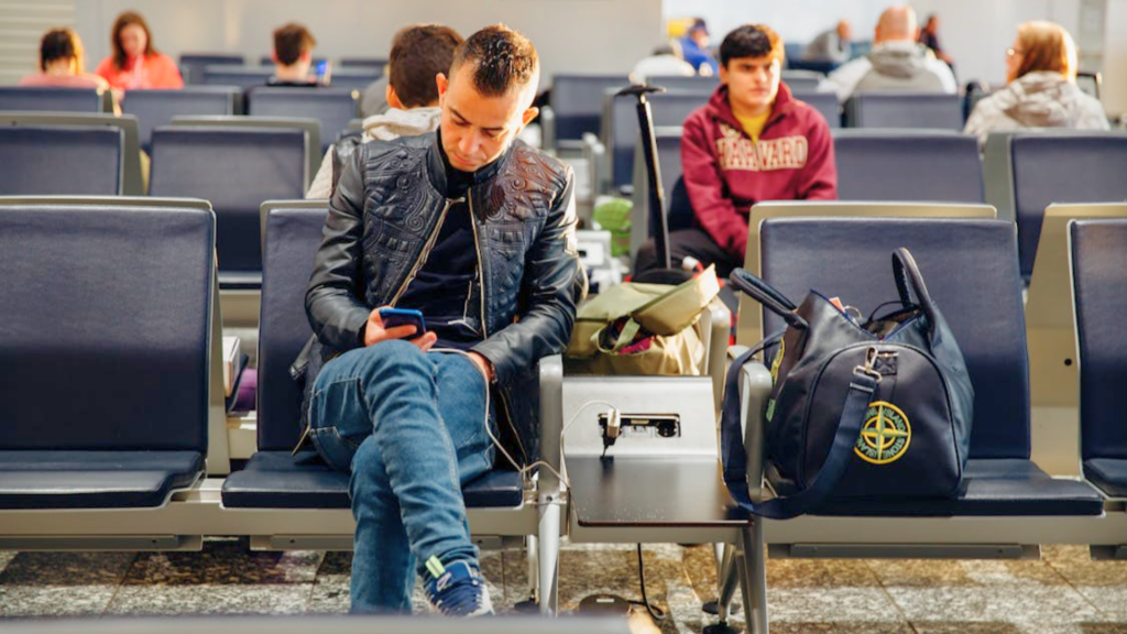 A man sits in an airport waiting area and looks at his smartphone.