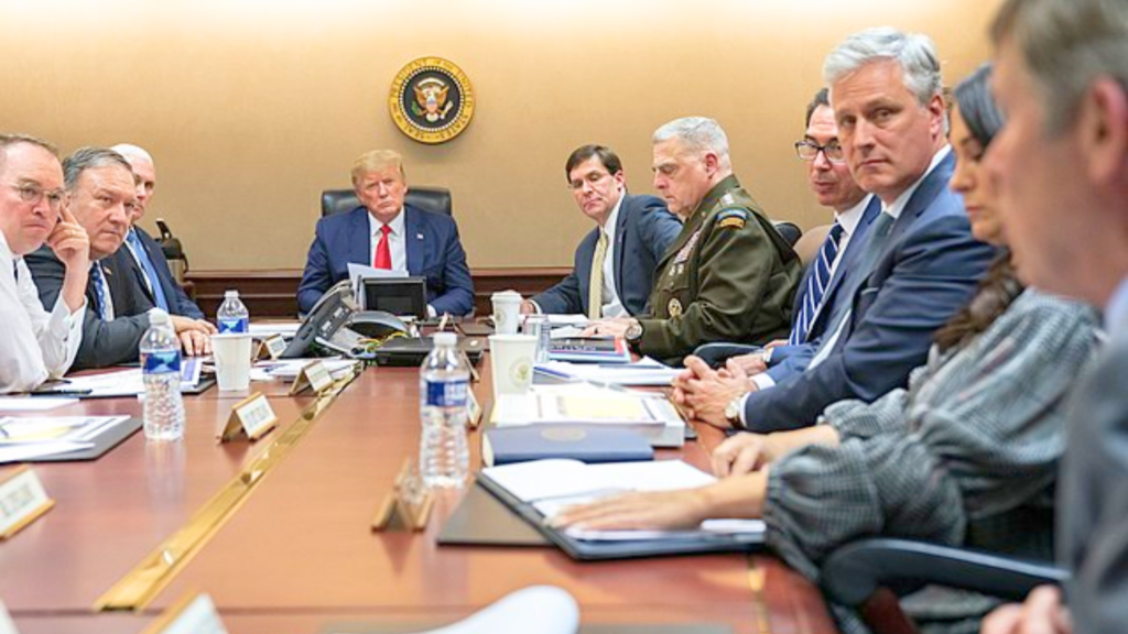 Donald Trump sits at the head of a long conference table during a meeting with several officials.