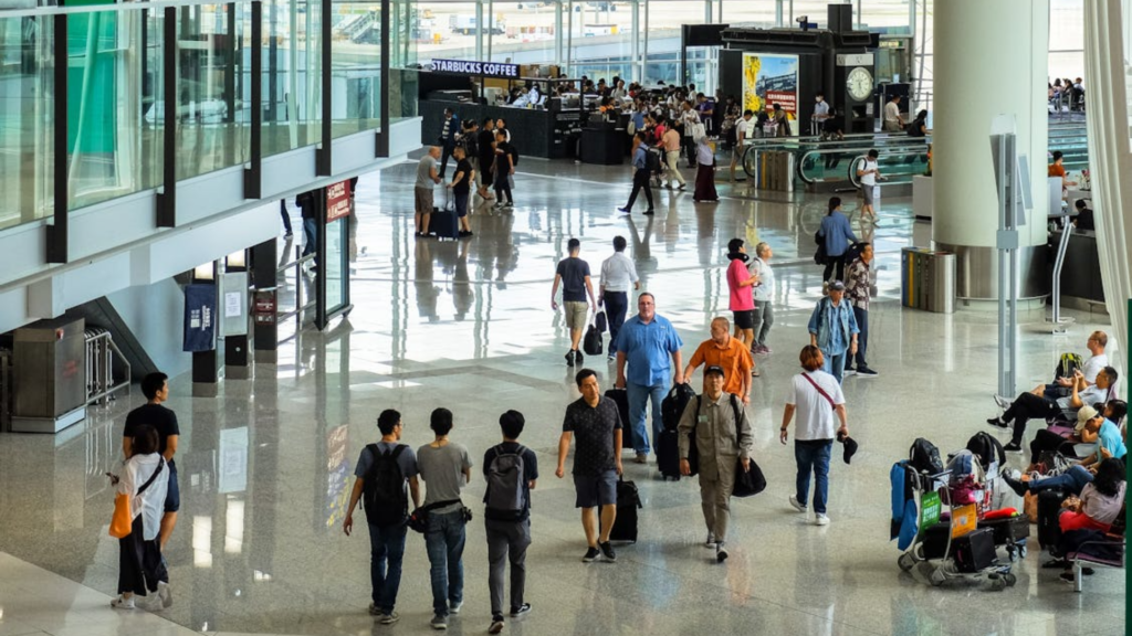 Many people walk with their luggage through a bright and busy airport.