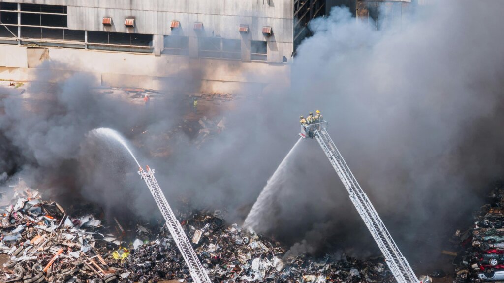 Firefighters spraying water on a large outdoor fire with heavy smoke.