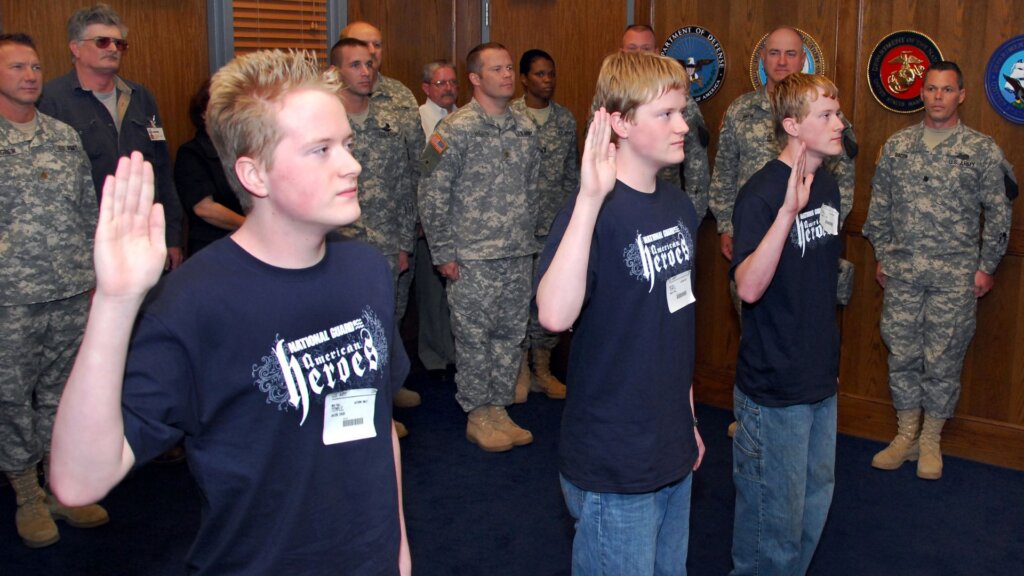 Teenagers raising their right hands during an enlistment ceremony with service members behind them.