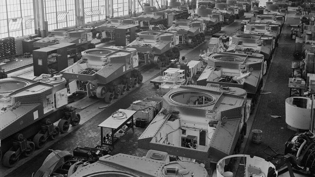 Assembly line producing military tanks inside a World War II-era factory.