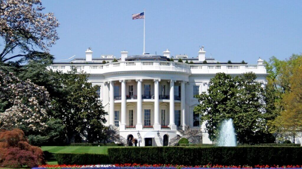 The White House exterior with American flag flying above the building and fountain on the South Lawn.