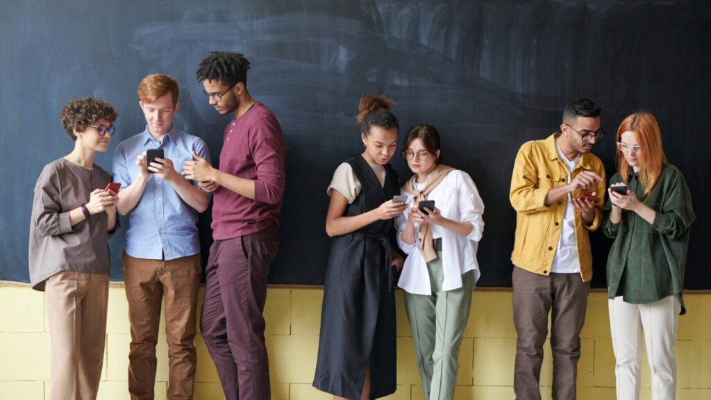 Group of young people standing together looking at smartphones against a studio backdrop.