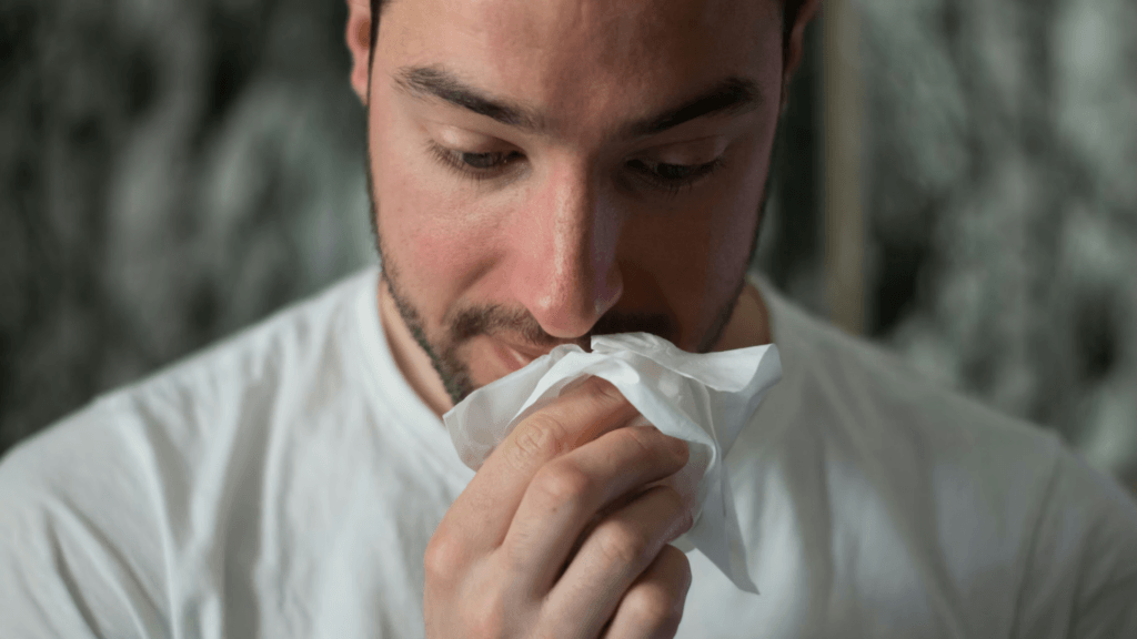 A man holds a white tissue up to his nose to wipe it.