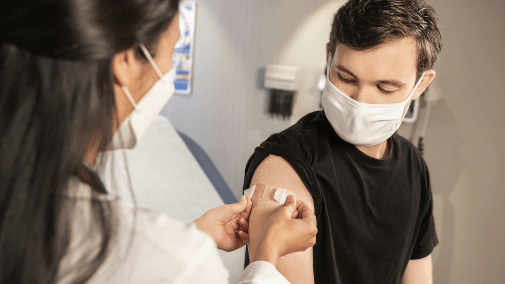 A healthcare worker wearing a mask puts a bandage on a man's arm.