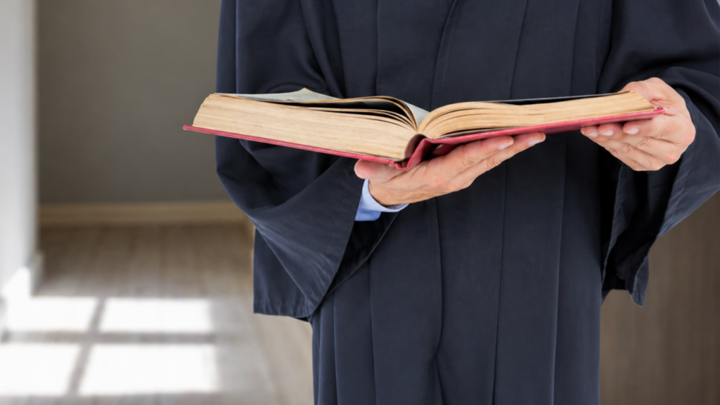 Clergy member holding open book, likely Bible, during indoor reading.
