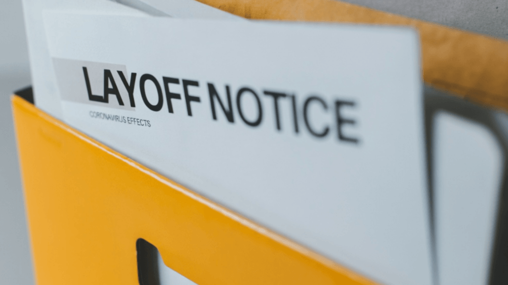 A close-up of a white document in a yellow folder that reads "LAYOFF NOTICE".