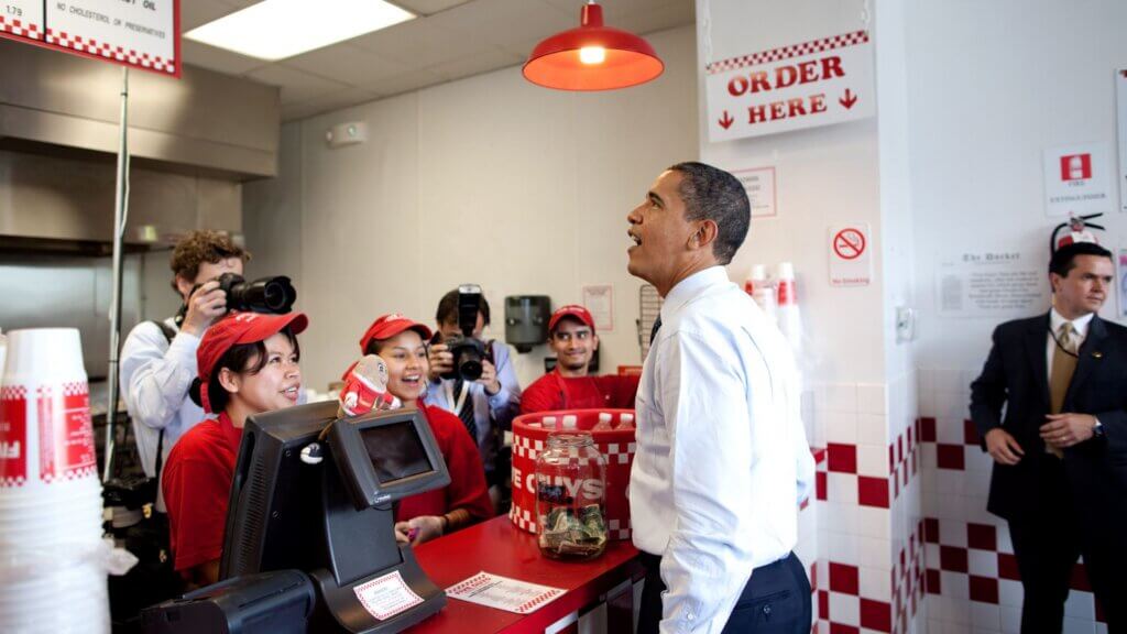 President Barack Obama speaking with Five Guys employees at restaurant counter during visit.