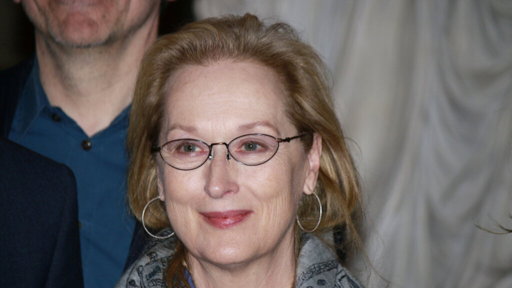 Meryl Streep smiling while wearing glasses at a public event.