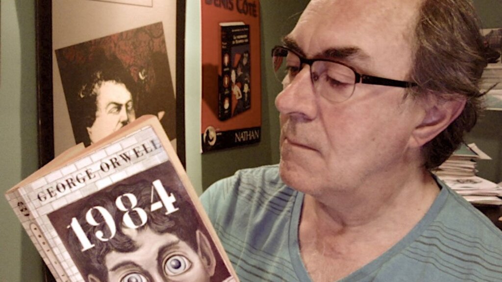 Man holding George Orwell’s 1984 book while looking at its cover indoors.