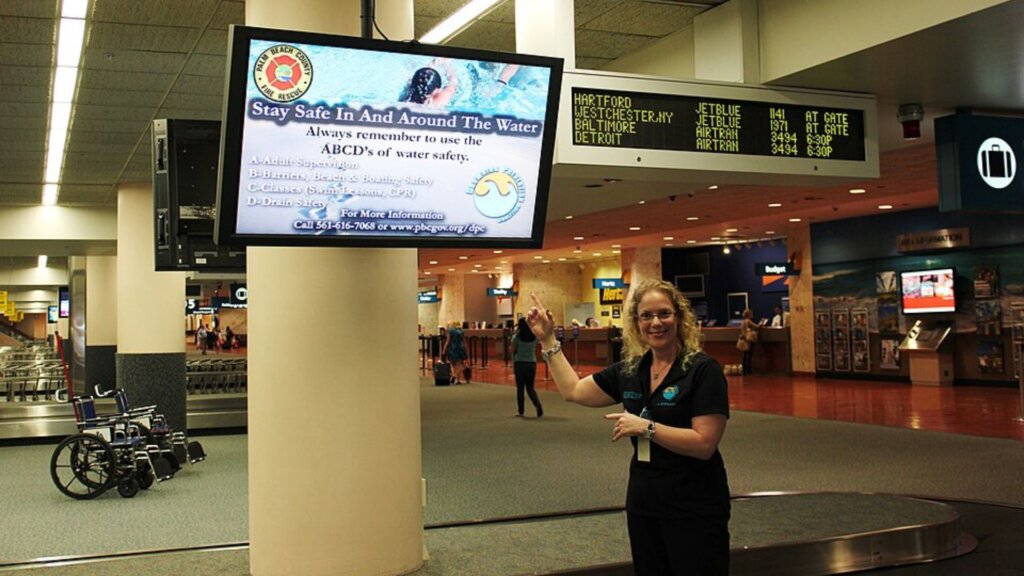 A woman inside an airport points up at a digital screen.