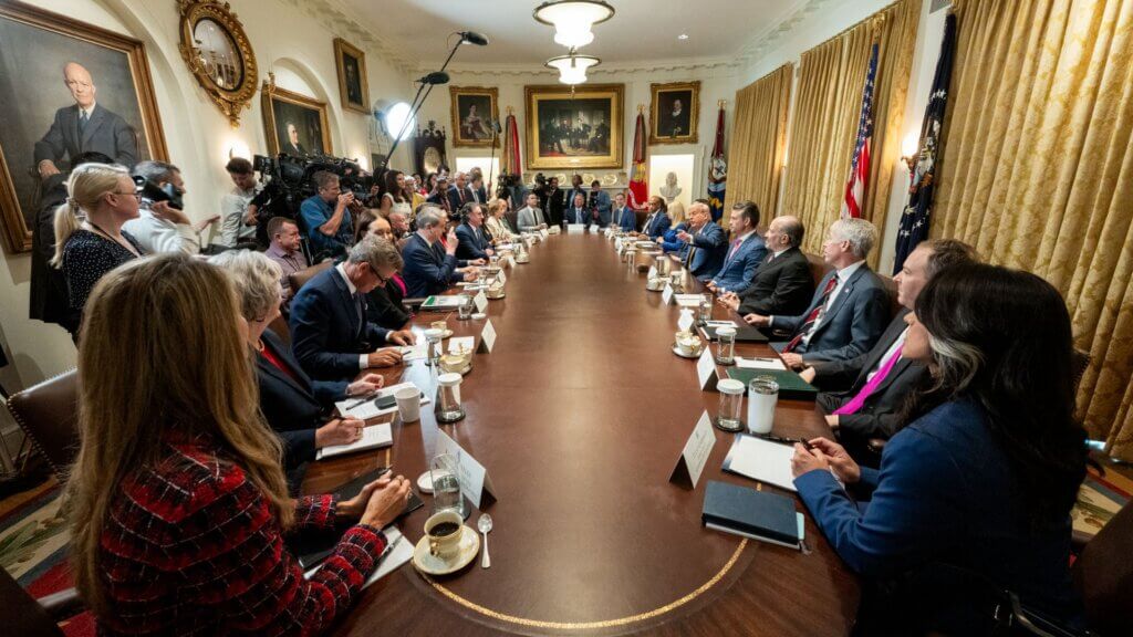 Donald Trump meeting with officials and media around a conference table in the White House Cabinet Room.