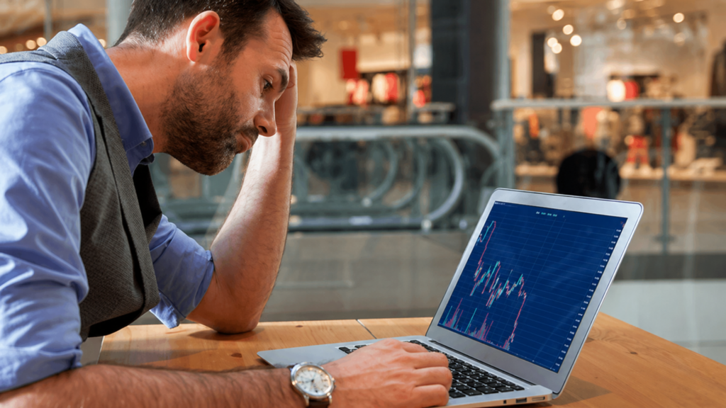 Man looking concerned while viewing declining stock chart on laptop.