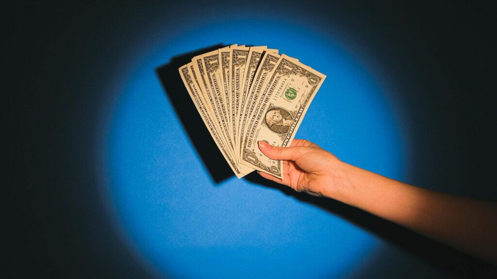 Hand holding a fan of US dollar bills against a blue background.