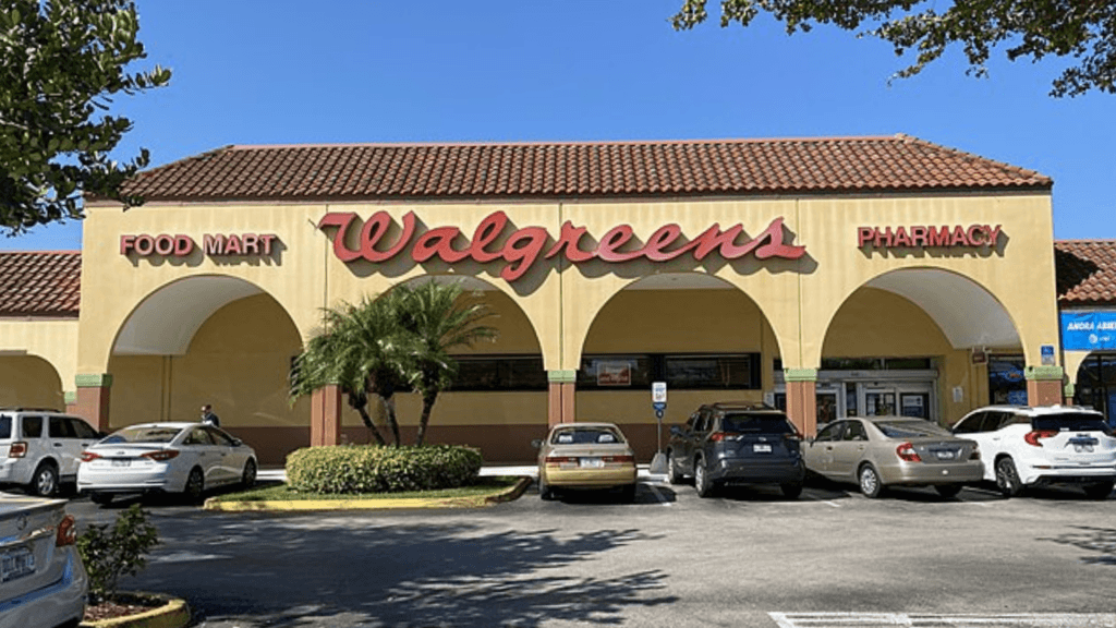 A Walgreens storefront with a Spanish-style red tile roof and arched entryways, located behind a parking lot filled with cars.