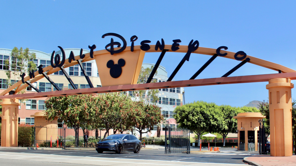 A black car drives through the arched entrance of The Walt Disney Co. studios, which features the company name in script and a Mickey Mouse silhouette