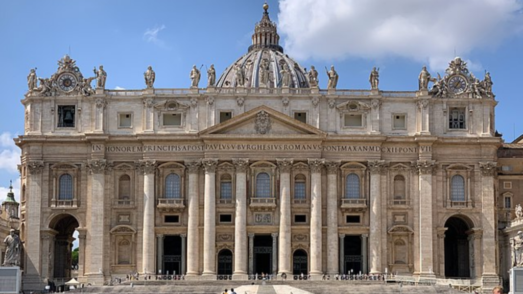 A wide shot of the grand, pillared facade of St. Peter's Basilica under a blue sky in Vatican City.
