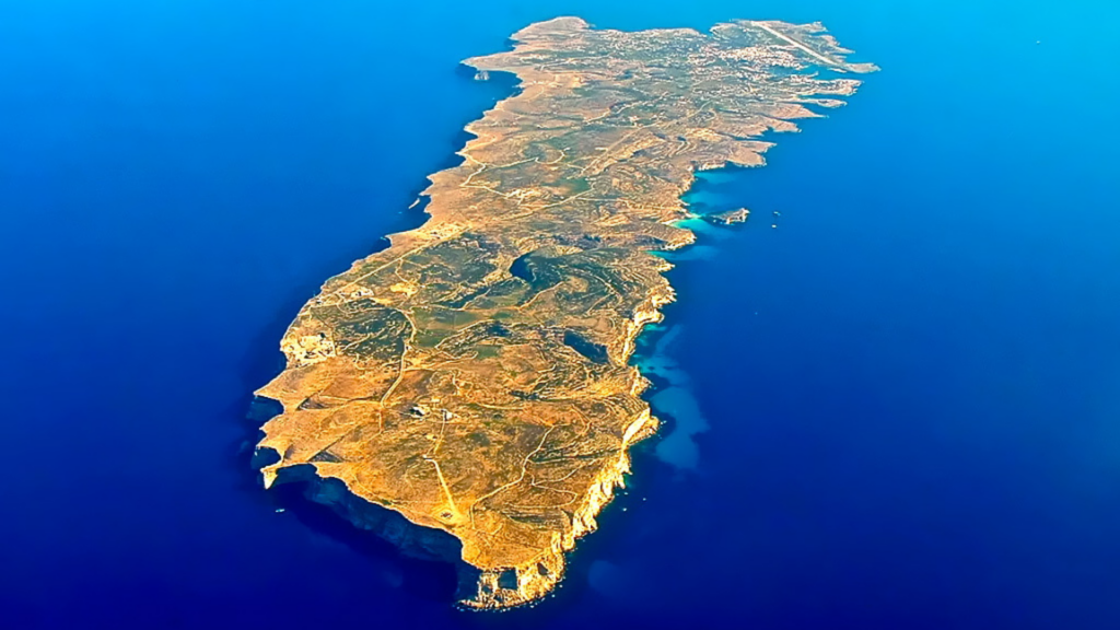 An aerial view shows a long, rocky island surrounded by deep blue ocean water.
