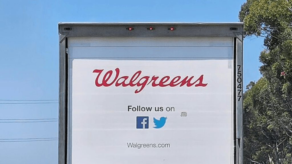 The rear view of a white Walgreens semi-truck on a highway, featuring the company logo and social media icons.