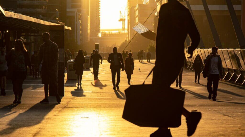 Silhouettes of people walking along a busy city street.