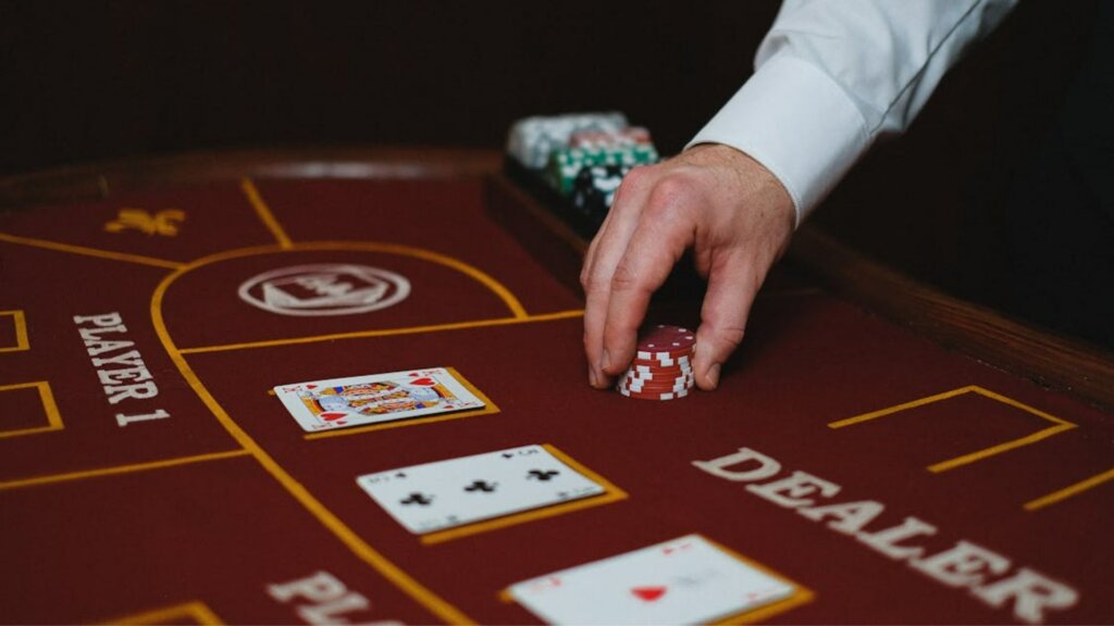 A dealer's hand stacking red chips on a casino card table with playing cards.