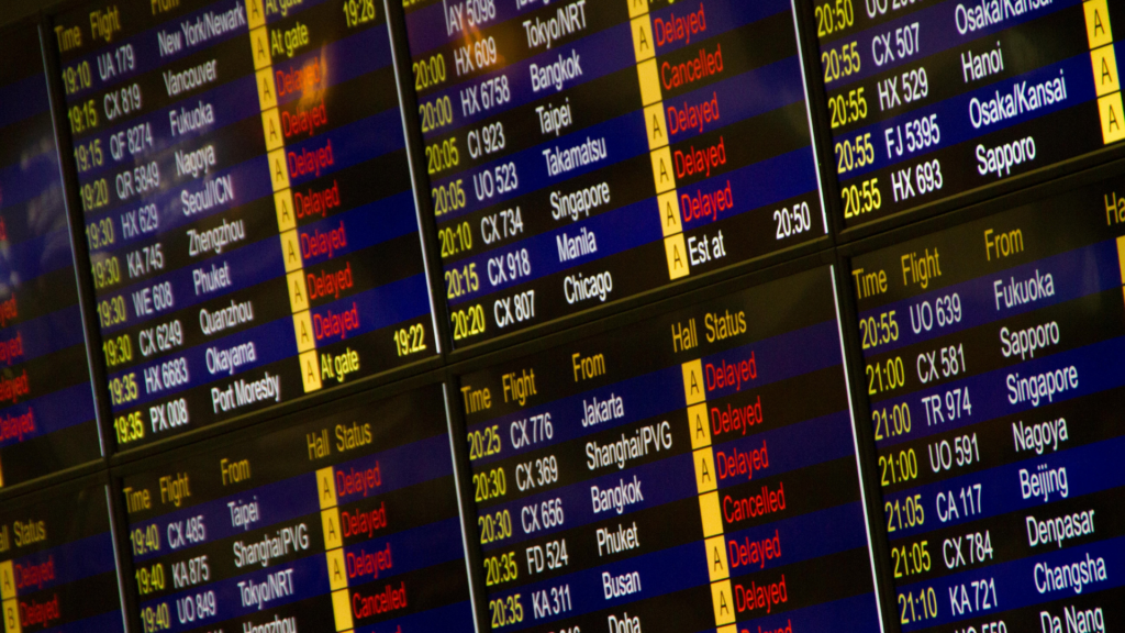 A close-up view of a digital airport departure board displays a long list of flight times, destinations, and gate statuses in glowing text.