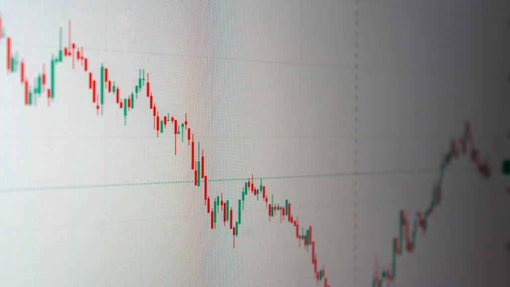 A close-up view of a digital screen displays a financial candlestick chart with red and green bars indicating downward and upward price fluctuations over time.