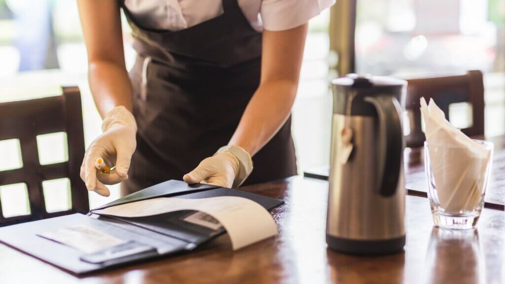 Restaurant server in apron and gloves handling a check at a table.