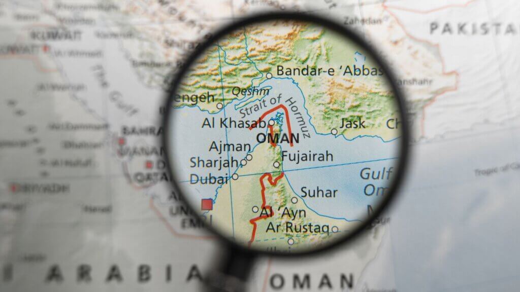 Magnifying glass focused on a map of the Strait of Hormuz between Iran and Oman.