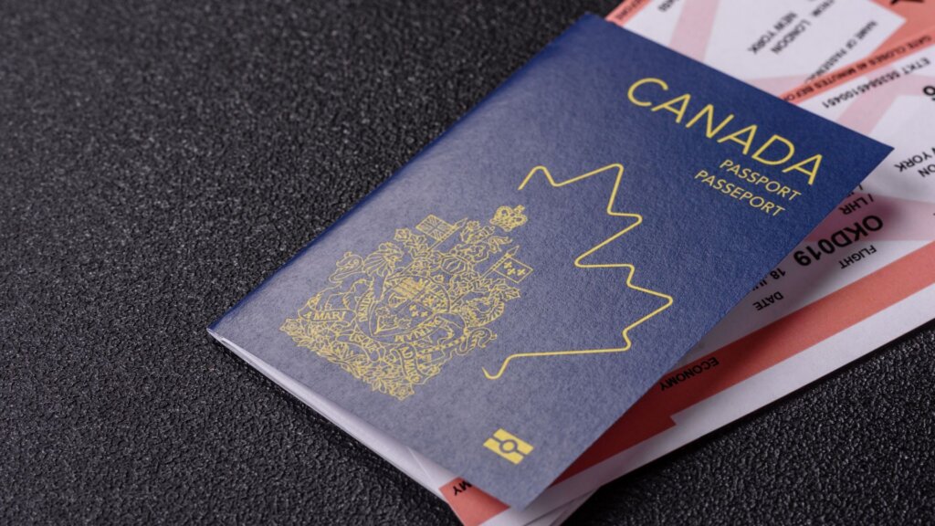 Canadian passport resting on airline tickets on a textured dark surface. The passport is blue with a gold maple leaf and emblem.