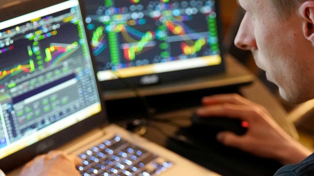 A person analyzes stock charts on two laptop screens, displaying colorful graphs and data.