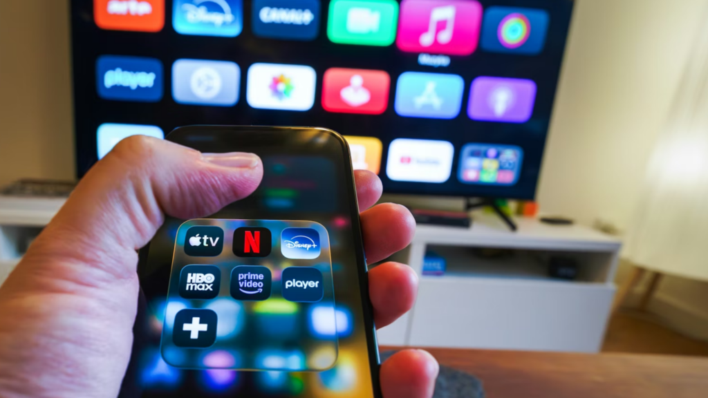 A first-person view of someone holding a smartphone with a folder of streaming apps open, including Netflix, Disney+, and HBO Max.