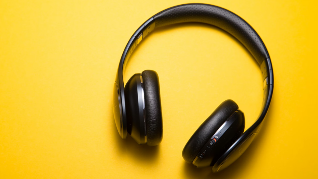 A pair of black over-ear wireless headphones resting on a bright, solid yellow background.