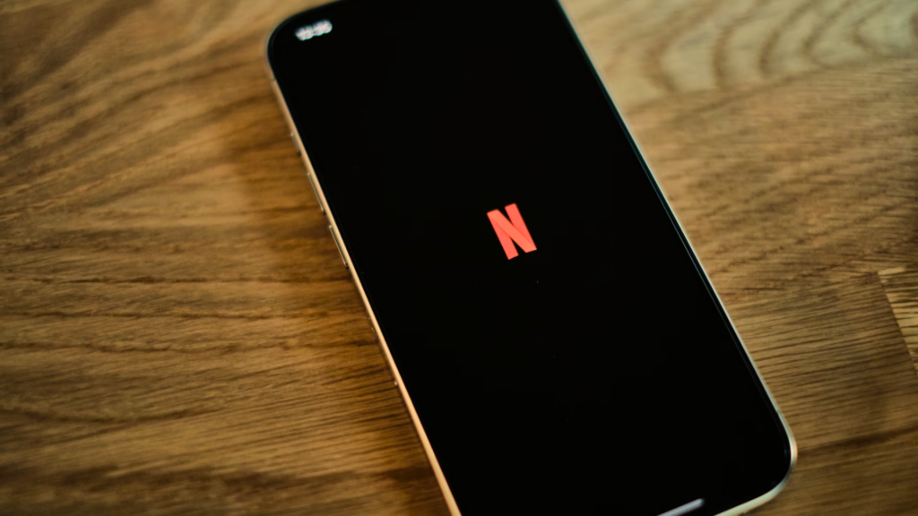 A top-down shot of a smartphone resting on a wooden surface, displaying the red Netflix _N_ logo on its screen.