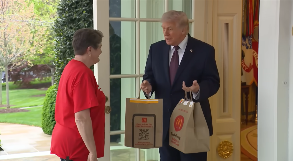 Donald Trump holding McDonald’s takeout bags while speaking to a woman at a doorway.