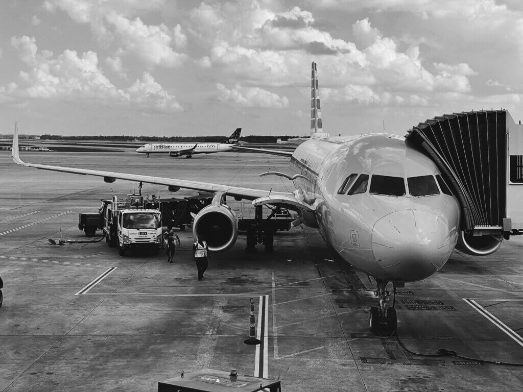 Airplane parked at airport gate with jet bridge and ground crew nearby.