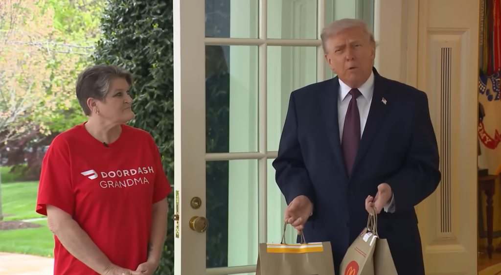 Donald Trump holding McDonald’s takeout bags while standing beside a DoorDash delivery worker.
