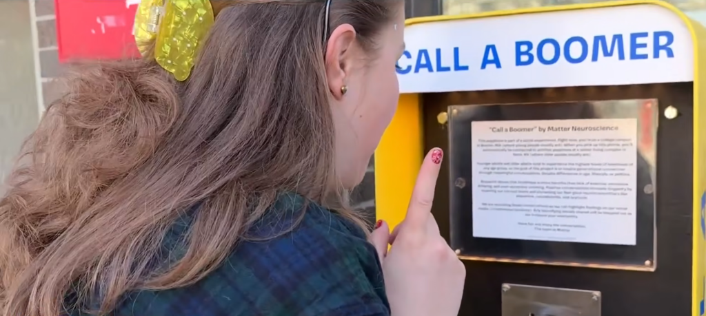 Woman reading instructions on a “Call a Boomer” public payphone.